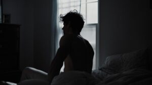 Person sits on bed with light from window