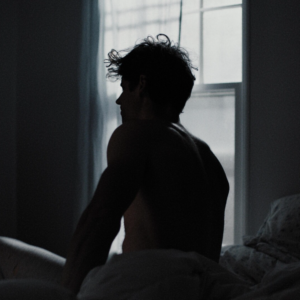 Person sits on bed with light from window