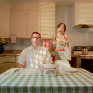 Two people sitting at kitchen table look towards camera