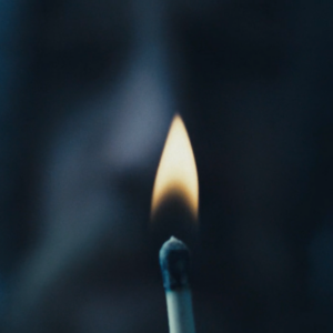 Close up of match with face behind.