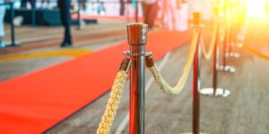 Wide panoramic view rope fencing with gold pillars with a red carpet for celebrities and guests of an expensive event with crowds of people