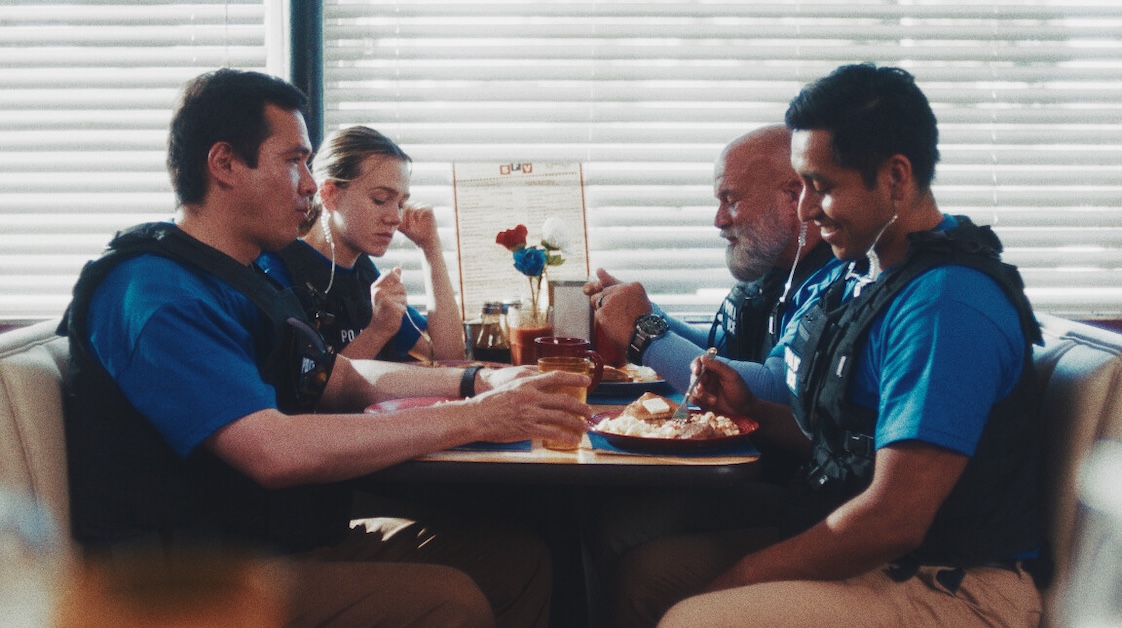 Image of four people wearing blue shirts and police vests sitting and eating and smiling.