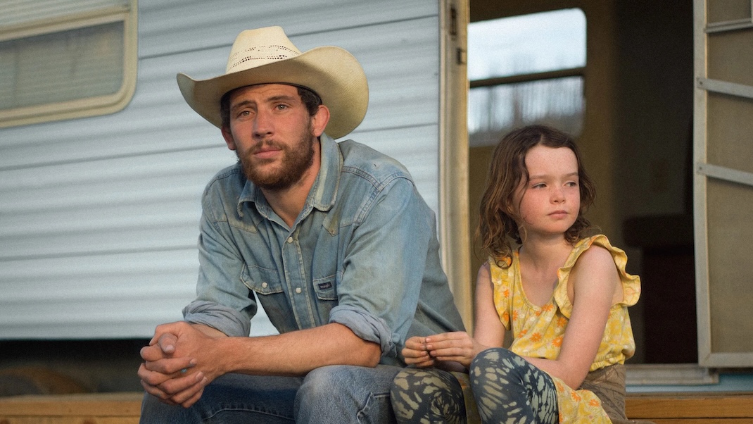 Image of a adult with cowboy hat sitting outside with young kid.