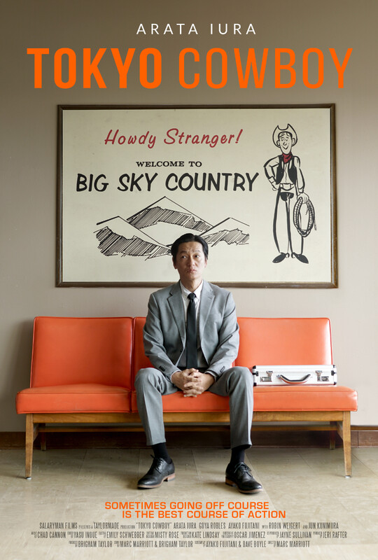Tokyo Cowboy Poster A man sits on a bright orange couch. Above him hangs a poster that says "Big Sky Country".