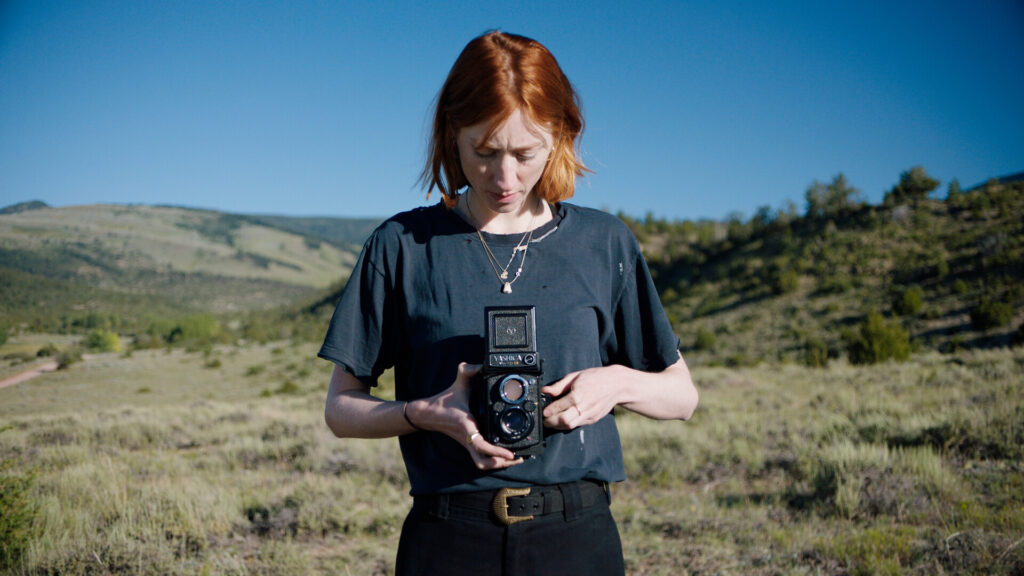 Person standing outside in dark shirt looking down at top viewfinder of camera