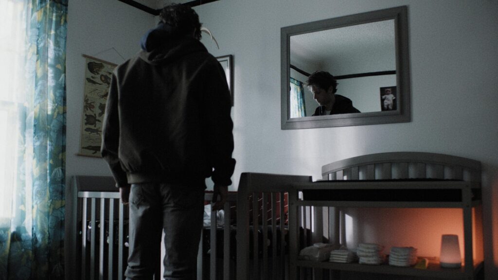 Person in coat looks down on crib.