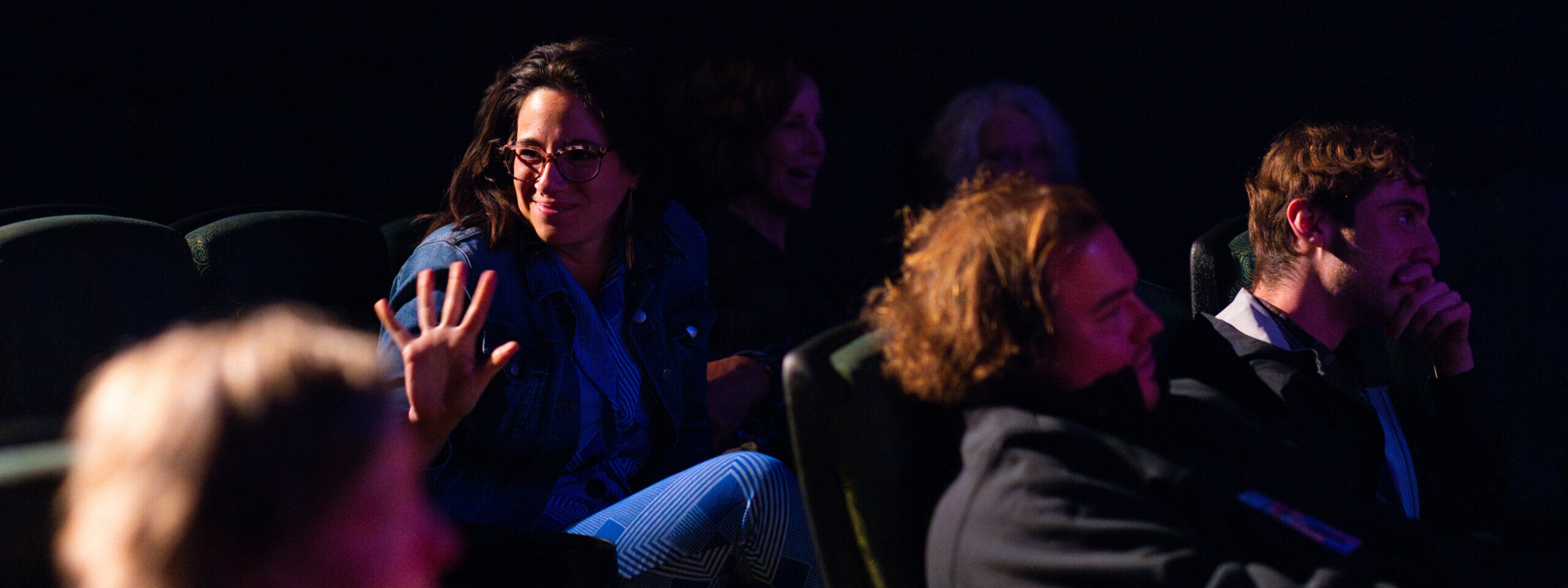 MTFF-DayFour-26 Person in dark theater waves while other look right.