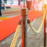 Wide,Panoramic,View,Rope,Fencing,With,Gold,Pillars,With,A Wide panoramic view rope fencing with gold pillars with a red carpet for celebrities and guests of an expensive event with crowds of people