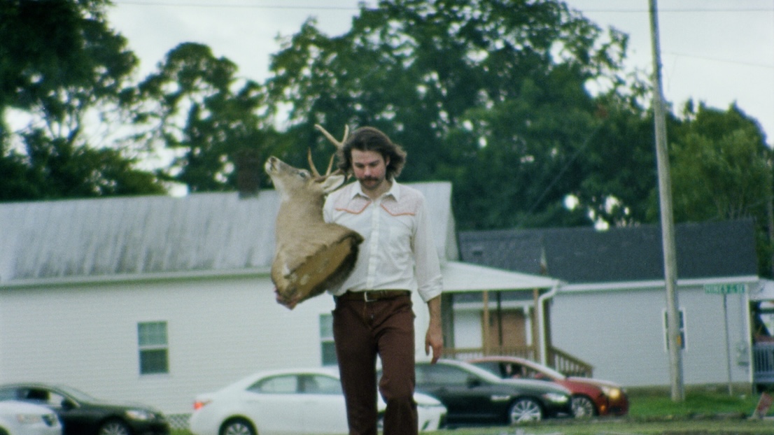 BMI_4-scaled Image of person holding taxidermy deer head outside.