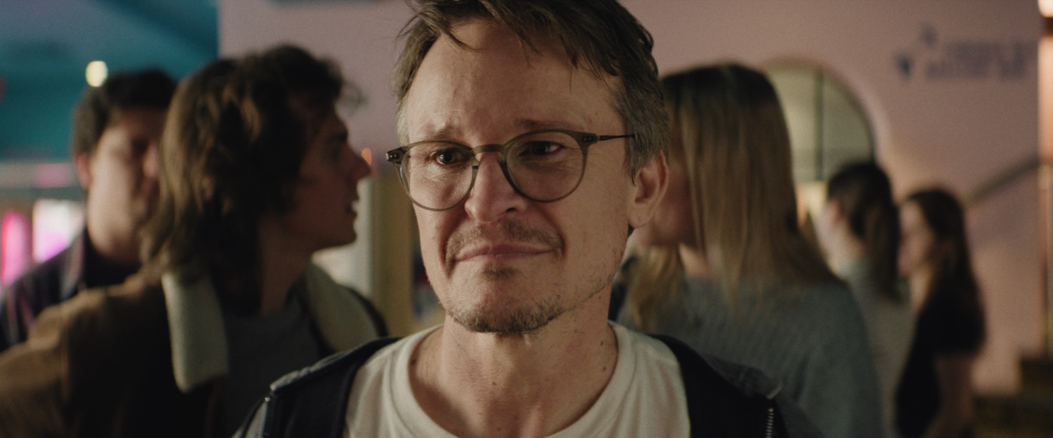 Image of a person with glasses in a crowd looking toward camera.