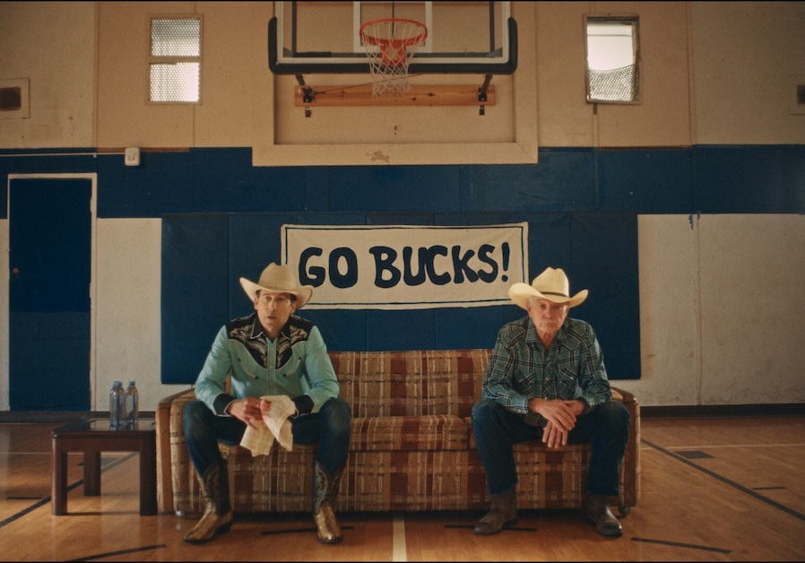 RAH3 Image of two people in cowboy hats sitting on a couch in a gym under a basketball hoop.