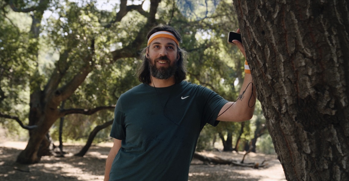Image of a person leaning against a tree with headphones on and a headband on.