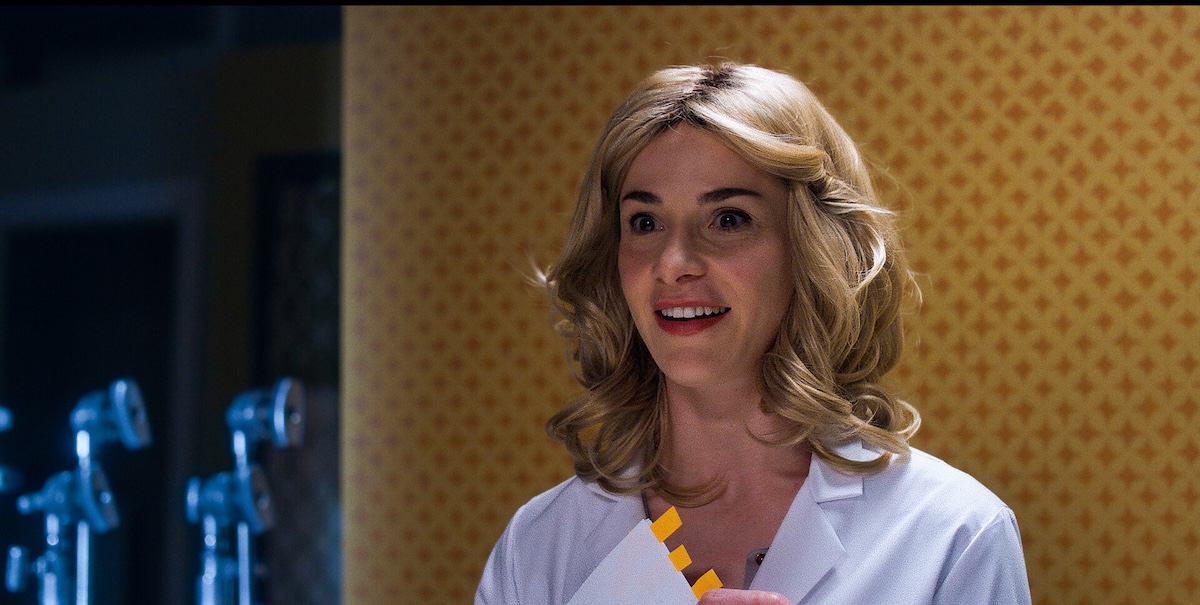 Image of person smiling in front of yellow pattern with c-stands on the side.