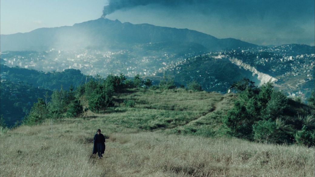 Image of landscape with volcano with person walking in grass.