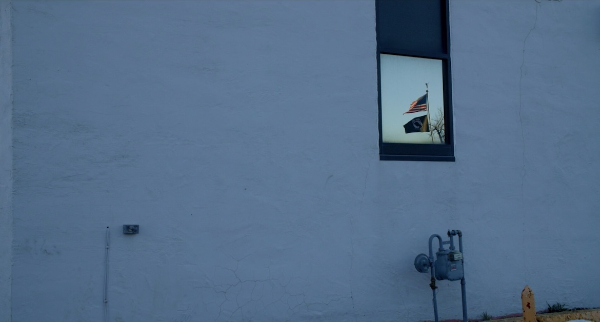 Image of wall of building with flags reflecting in window.