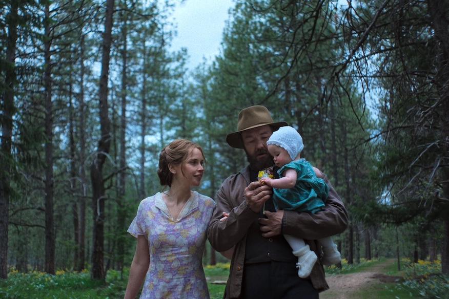 Image of two adults, one carrying a child, walking in woods.